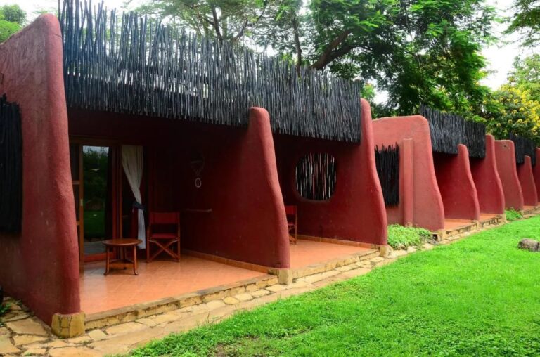 Terasy pokojů Amboseli Serena Safari Lodge mezi zaoblenými červenými zdmi, s výhledem na trávník