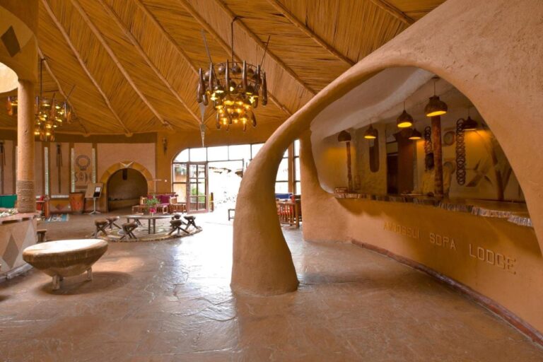 Recepční pult z tvarované hlíny s vyrytým názvem Amboseli Sopa Lodge, pod stropem z rákosu