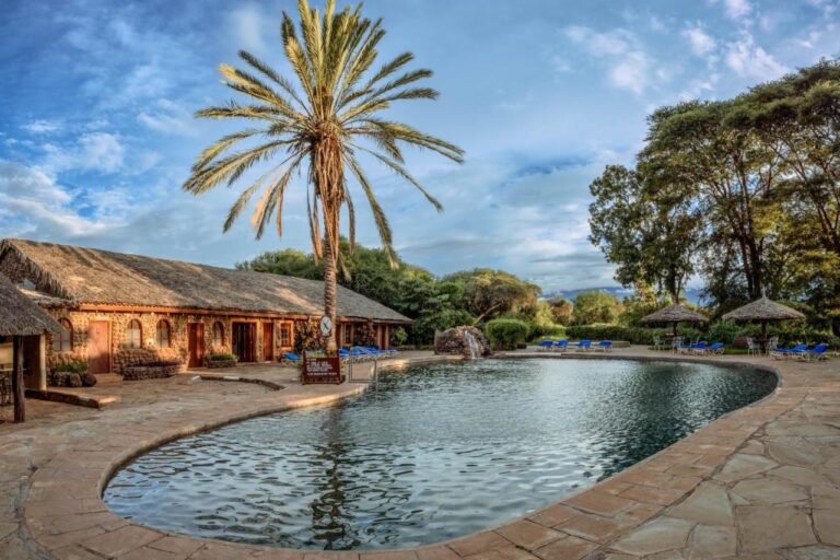 Bazén Amboseli Sopa Lodge s palmou, doškovými slunečníky a kamennou budovou