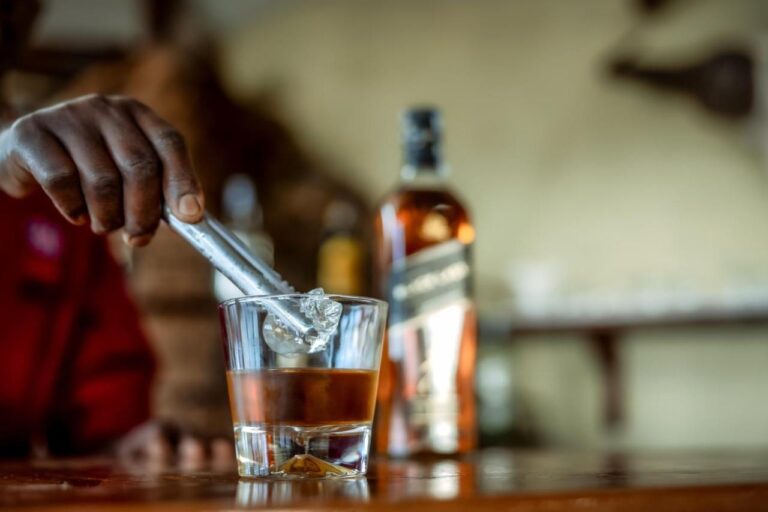Ruka vkládá kostku ledu do sklenice whisky na barovém pultu