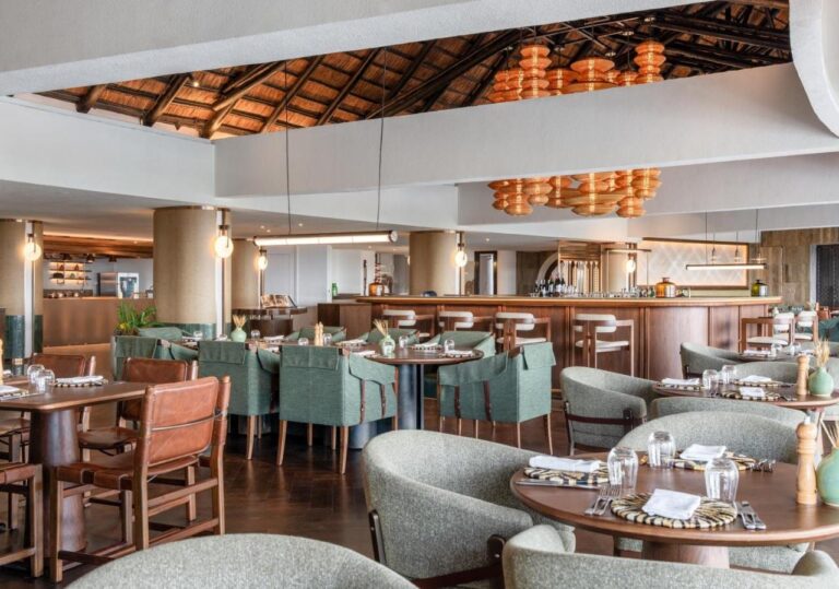 Restaurace se zelenými křesly před dlouhým barem, pod oranžovými závěsnými lampami