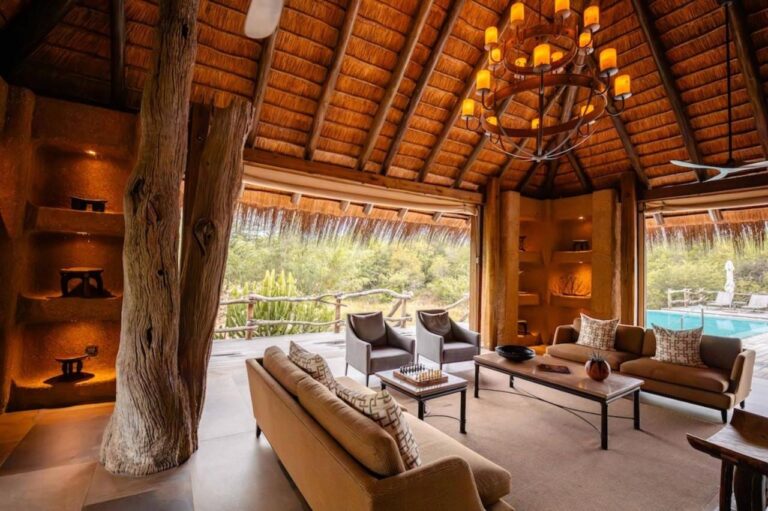 Salonek Kapama River Lodge pod vysokou doškovou střechou, otevřený na bazén a buš