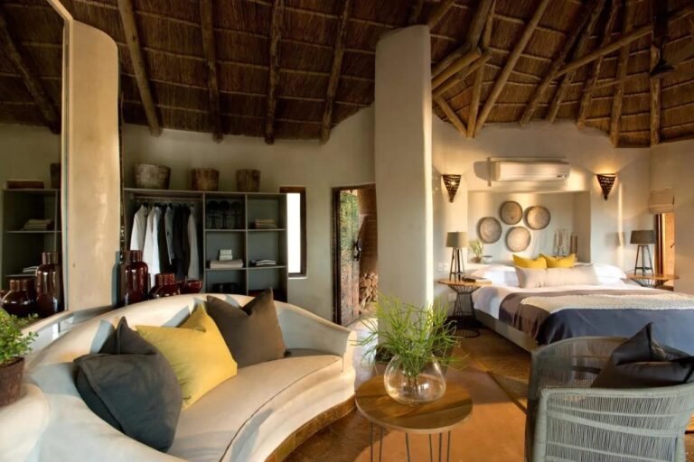 Apartmá Madikwe Safari Lodge se zaoblenou bílou pohovkou, velkou postelí a otevřenou šatní skříní