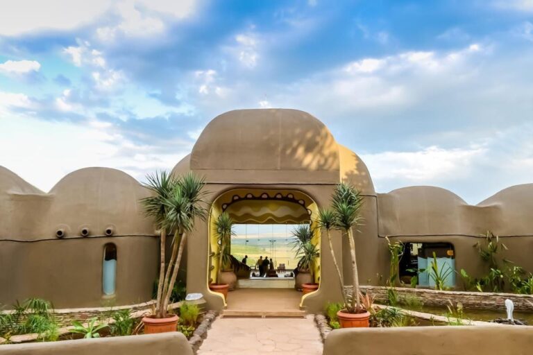 Vstup do Mara Serena Safari Lodge s hliněnými zdmi a kupolemi, otevřený do savany Masai Mara