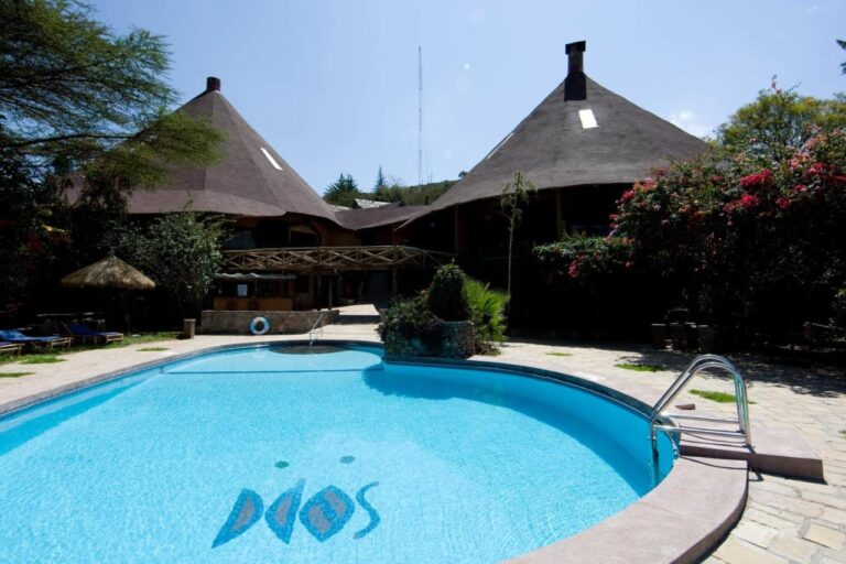 Bazén Mara Sopa Lodge před budovami s vysokými kuželovými doškovými střechami
