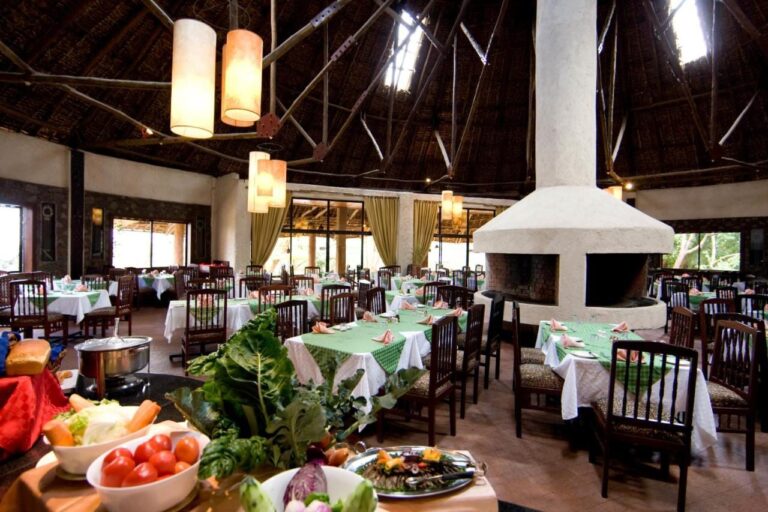 Restaurace se stoly se zelenými ubrusy a bufetem se zeleninou v popředí