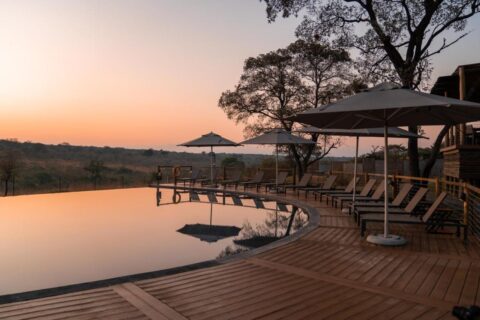 Infinity bazén Mdluli Safari Lodge pod oranžovou oblohou, lemovaný lehátky a slunečníky