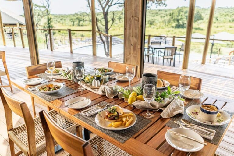 Prostřený stůl v restauraci, otevřené na terasu, bazén a buš