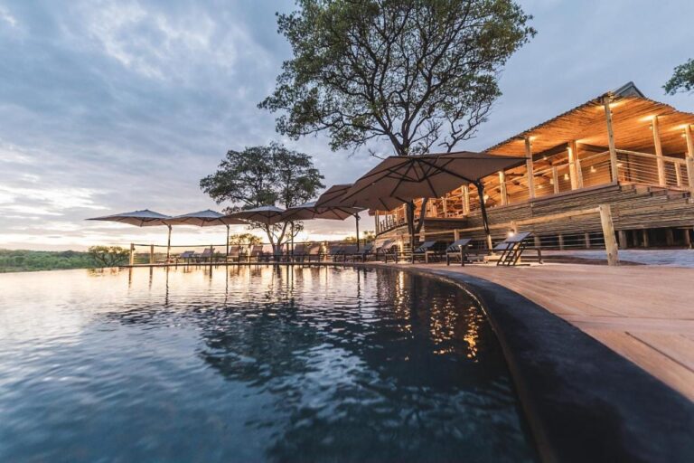 Infinity bazén Mdluli Safari Lodge a jeho osvětlená hlavní budova pod zataženou oblohou