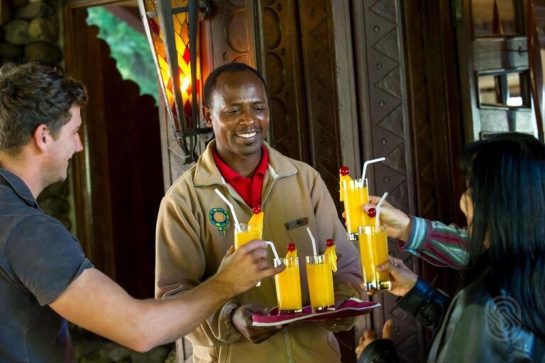 Zaměstnanec Ngorongoro Serena Safari Lodge podává dvěma cestovatelům podnos s ovocnými džusy