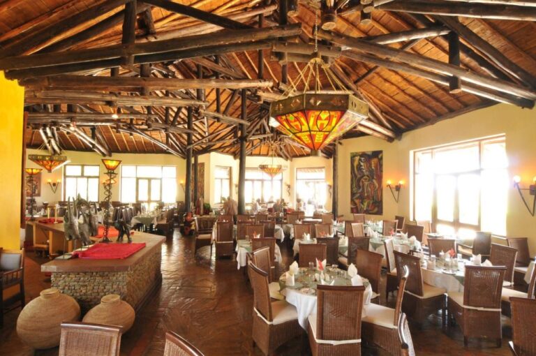 Jídelna restaurace pod krovem z kulatiny, s vitrážovými lustry a stoly s bílými ubrusy