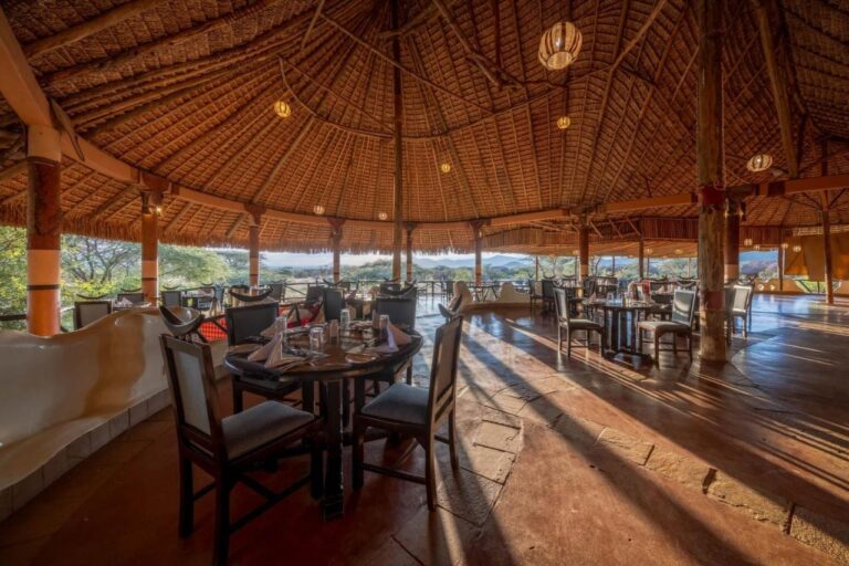Jídelna restaurace pod obrovskou doškovou střechou, otevřená na akácie a kopce