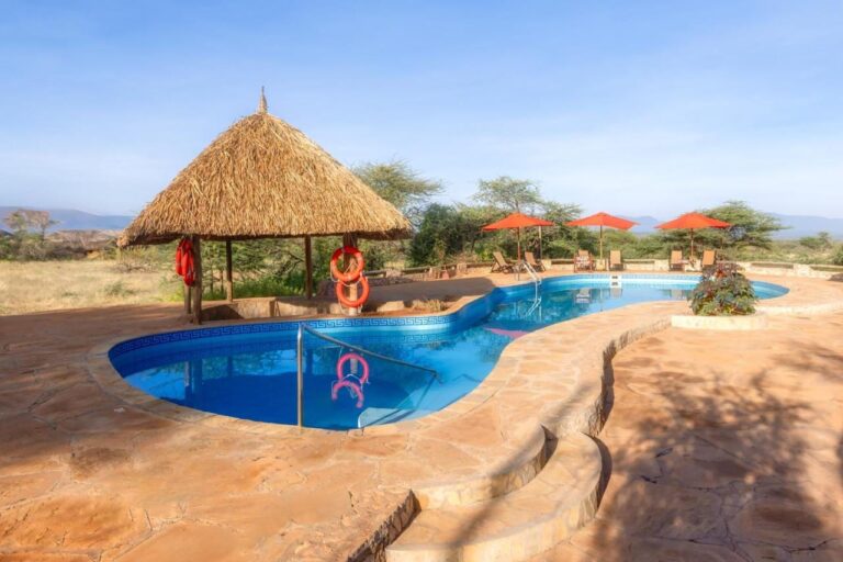 Bazén Samburu Sopa Lodge s doškovým přístřeškem, oranžovými záchrannými kruhy a červenými slunečníky, s výhledem do buše