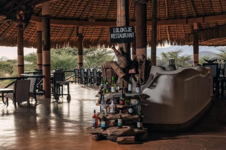Vchod do restaurace Lolokwe s lahvemi vína na kamenech, pod velkou doškovou střechou