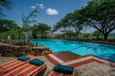 Infinity bazén Serengeti Serena Safari Lodge s červeně pruhovanými lehátky a zelenými ručníky pod akáciemi