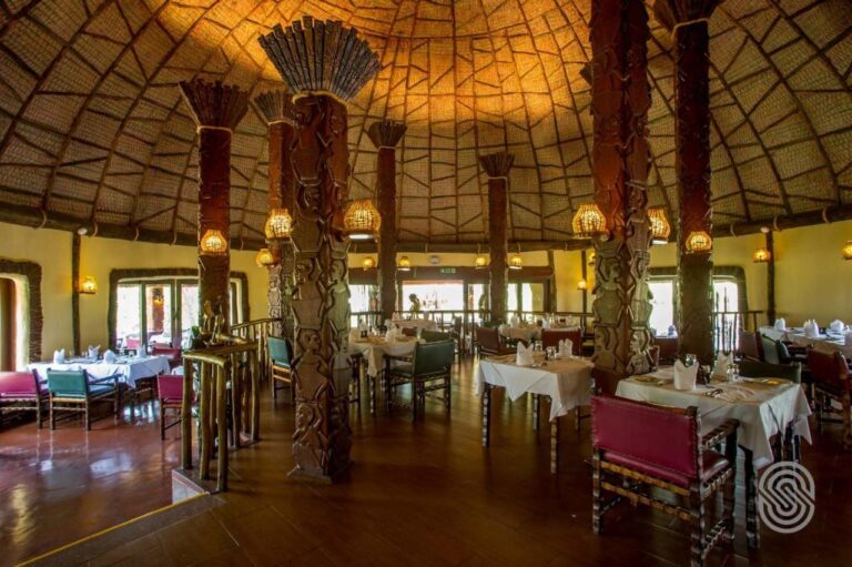 Jídelna restaurace pod kupolí, s dřevěnými sloupy s vyřezávanými postavami a stoly s bílými ubrusy