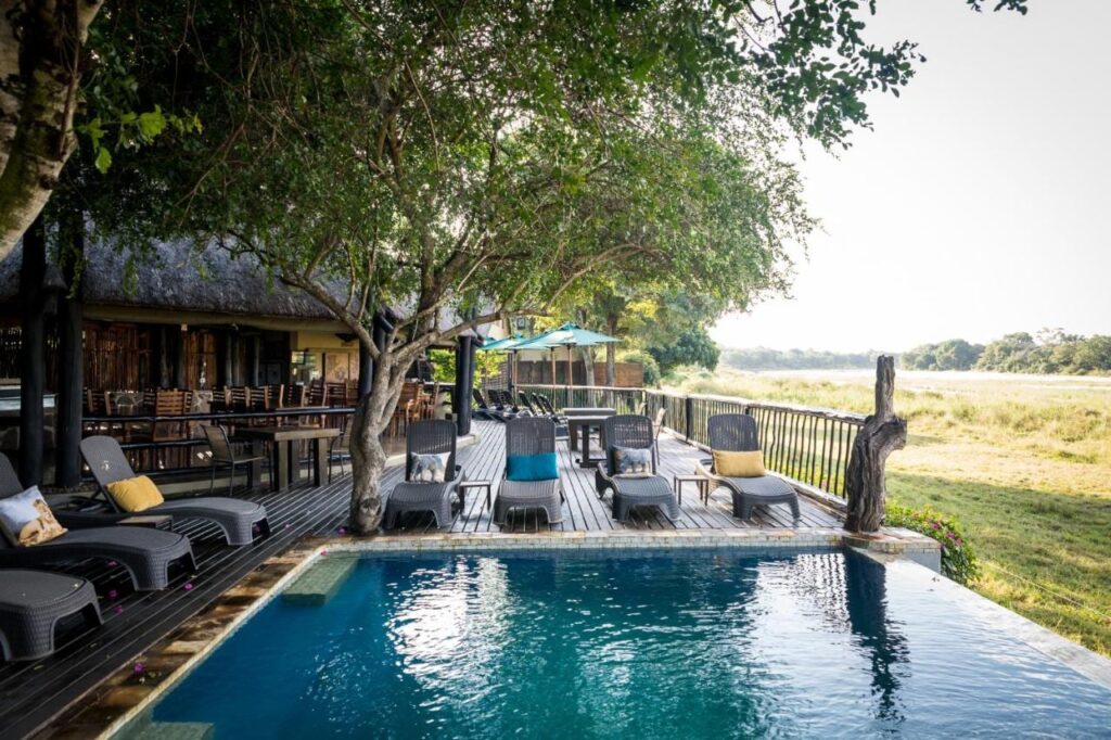 Bazén Umkumbe Safari Lodge a jeho dřevěná terasa nad travnatým břehem řeky