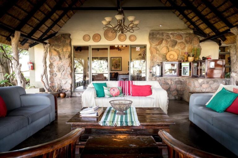 Otevřený salonek Umkumbe Safari Lodge pod doškem, se šedými pohovkami a kamennými zdmi